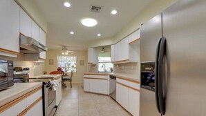 A modern kitchen with white cabinetry, a stainless steel refrigerator, and a built-in oven. - Long-term discount! Spacious 3BR Home With Tropical Garden & Koi Pond in Lanai (Punta Gorda)