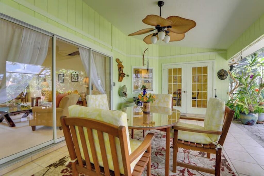 A room with a glass table, wooden chairs, a ceiling fan, and a view through a sliding glass door.