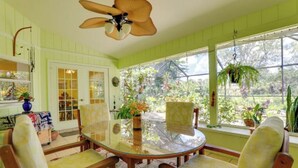A room with a glass table surrounded by wooden chairs, a ceiling fan, and large windows with plants. - Long-term discount! Spacious 3BR Home With Tropical Garden & Koi Pond in Lanai (Punta Gorda)