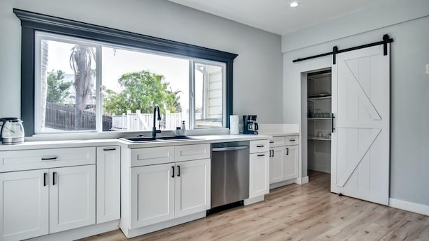 Una cocina moderna con armarios blancos, un ventanal grande y una puerta corredera estilo granja.
