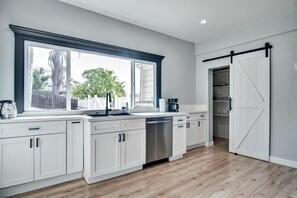 A modern kitchen with white cabinets, a large window, and a sliding barn-style door. - Ventura Downtown Minutes to Beaches (Ventura)