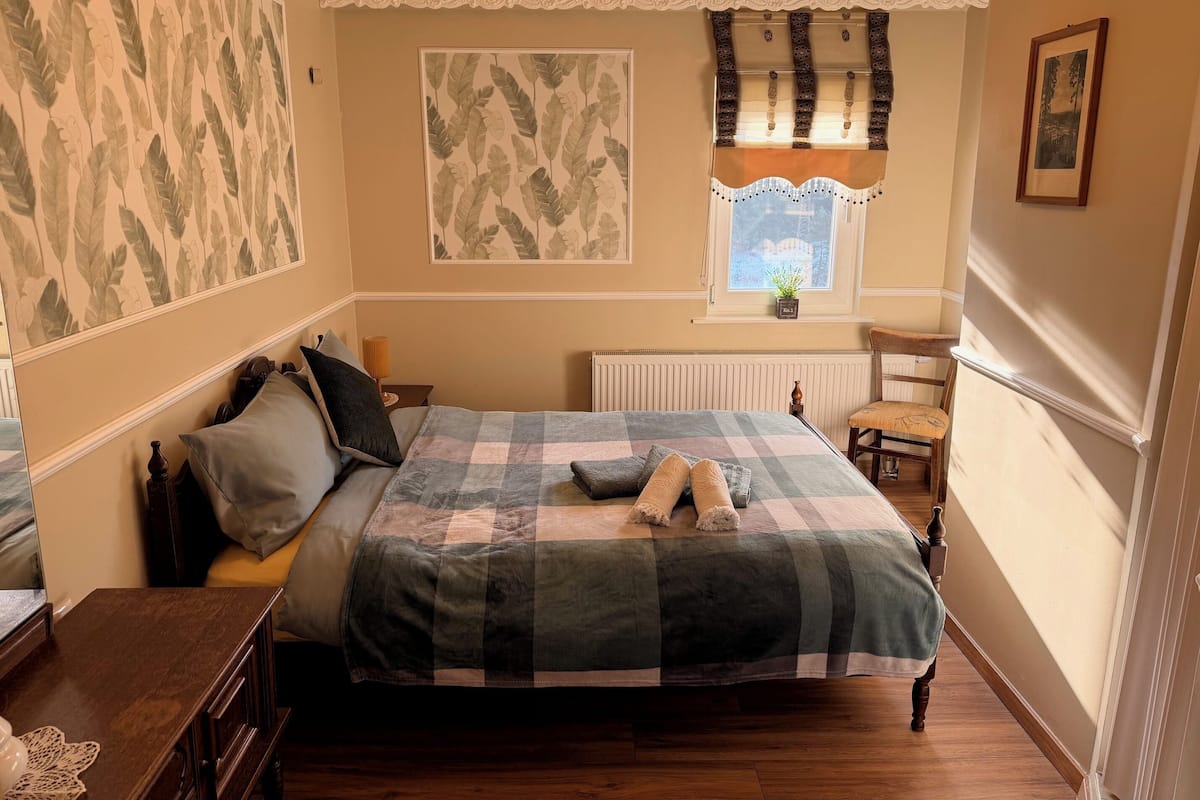 A bedroom with a bed, a nightstand, a chair, a window with curtains, and a chandelier.