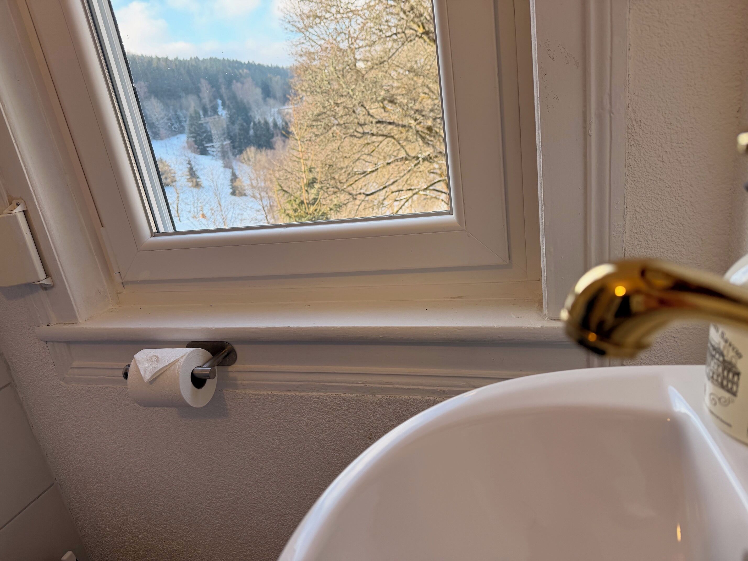 Un baño con ventana, un rollo de papel higiénico y un lavamanos.