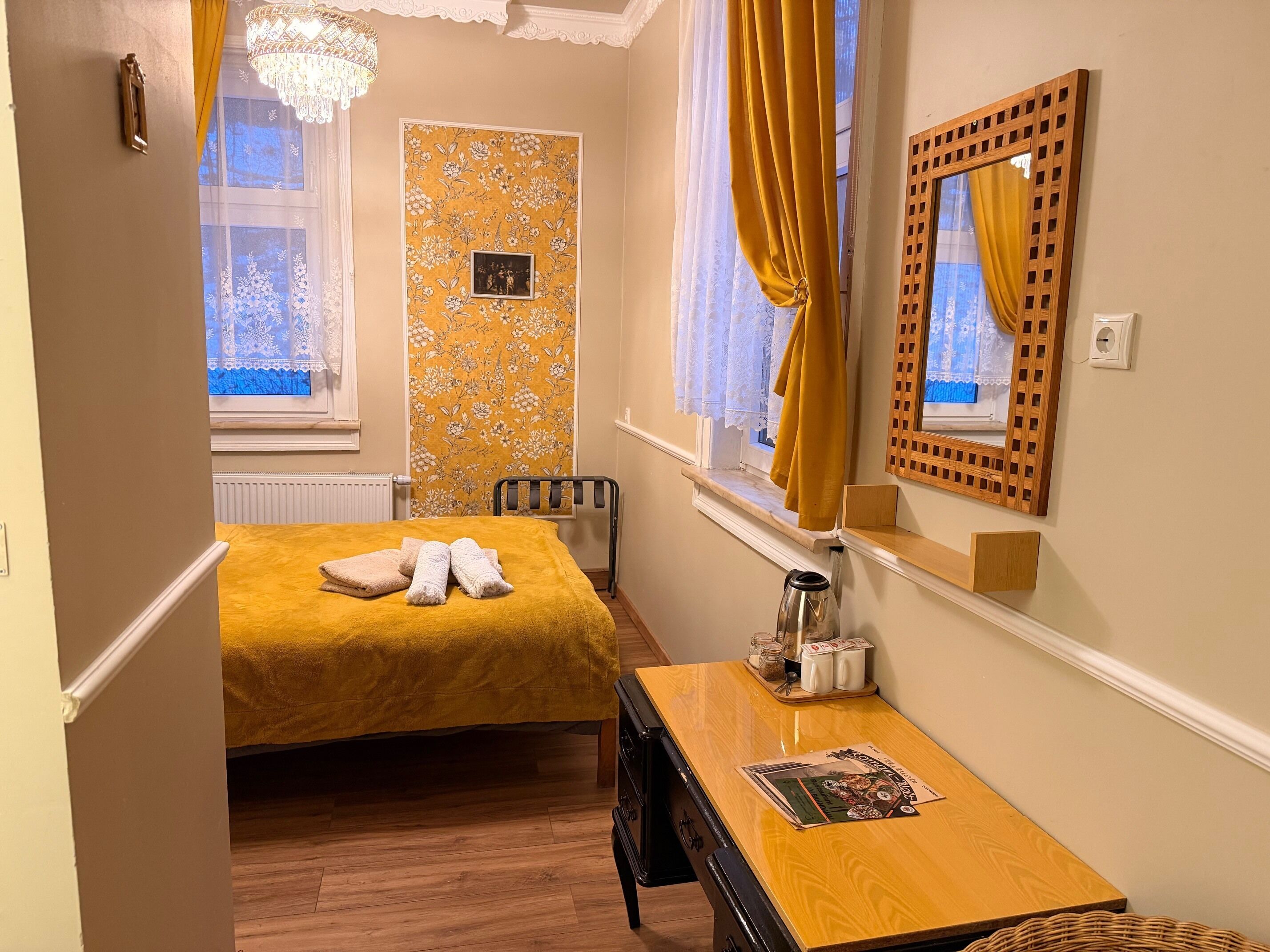 A bedroom with a bed, a bedside table with a kettle, salt and pepper shakers, and a mirror.