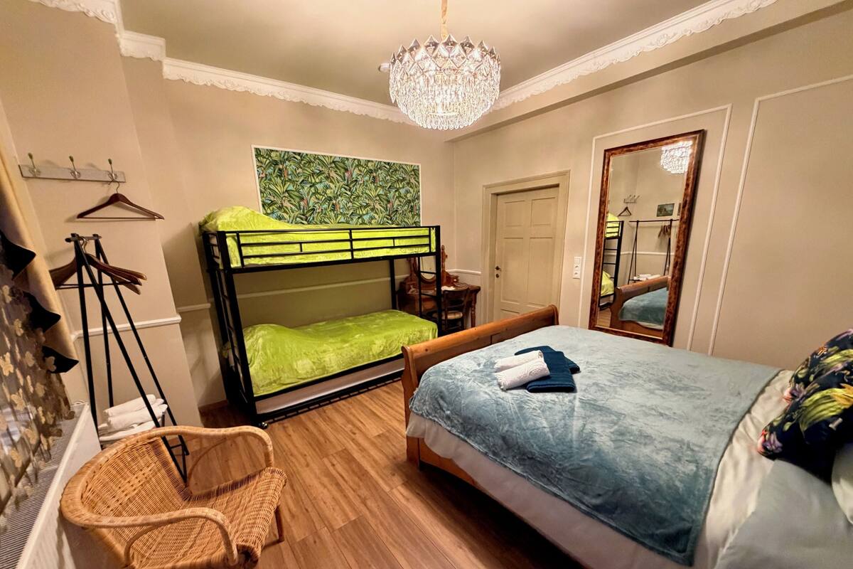 A bedroom with a bunk bed, a single bed, a chandelier, a mirror, and a wicker chair.