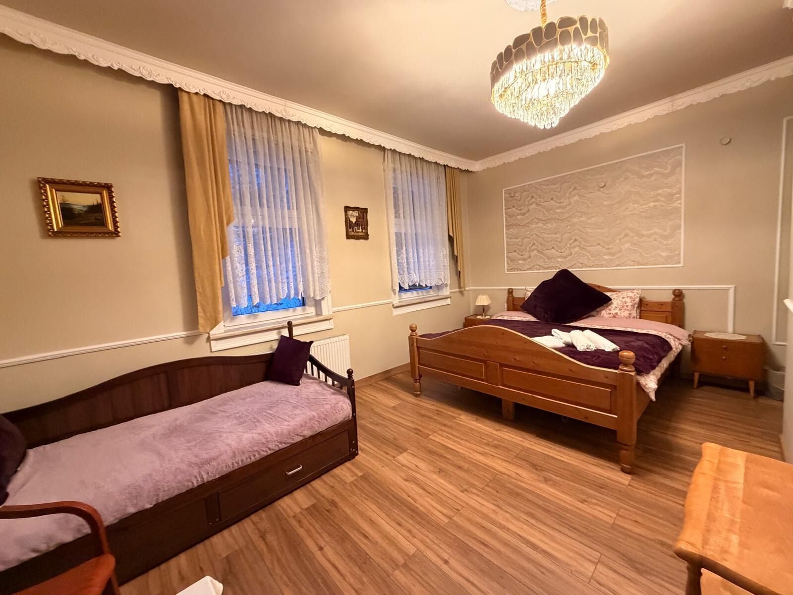 A bedroom with two wooden beds, a wooden chair, a small table, and a chandelier.
