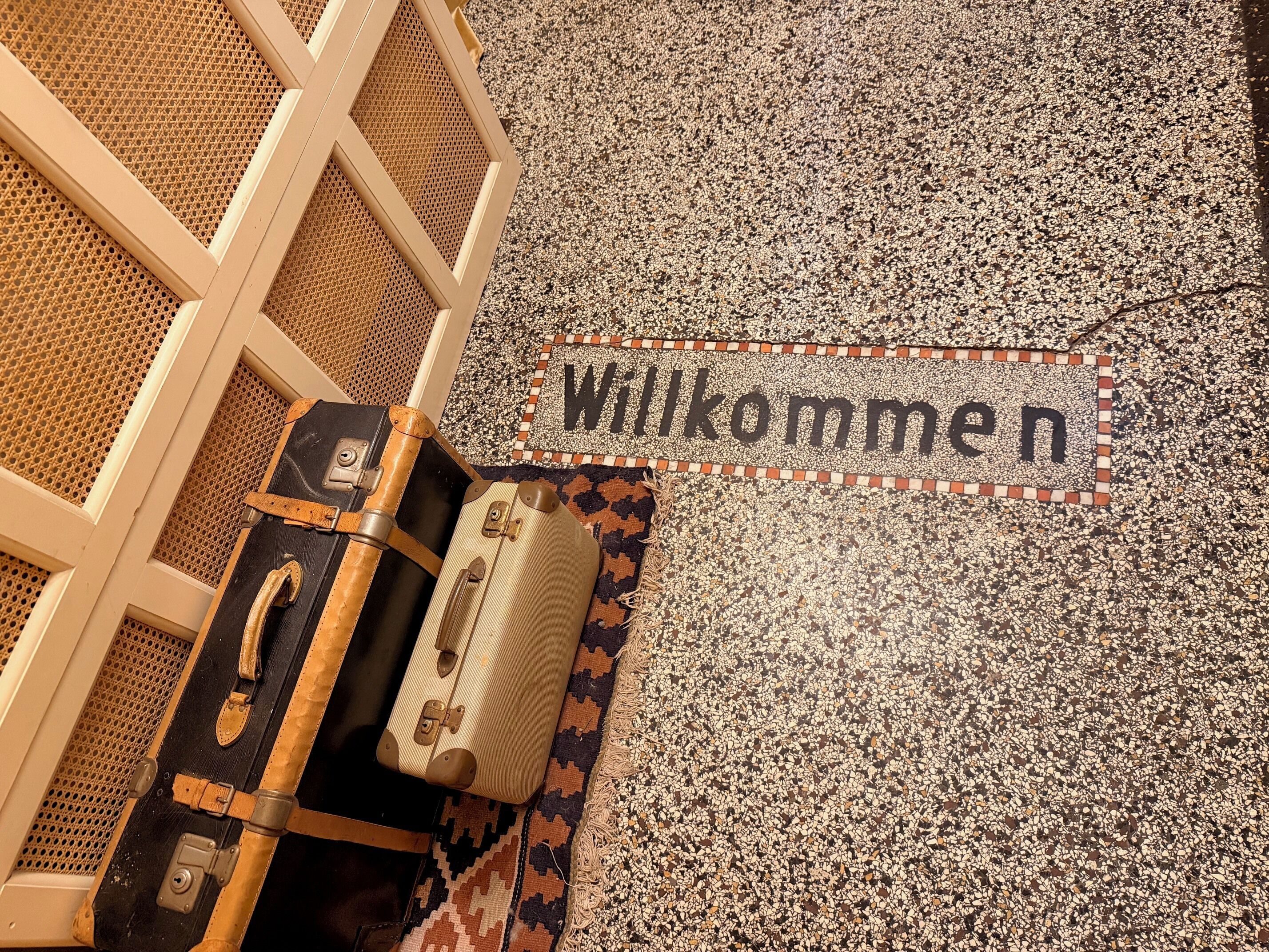 Un paillasson sur lequel est inscrit le mot « Willkommen » et qui repose sur un sol texturé.