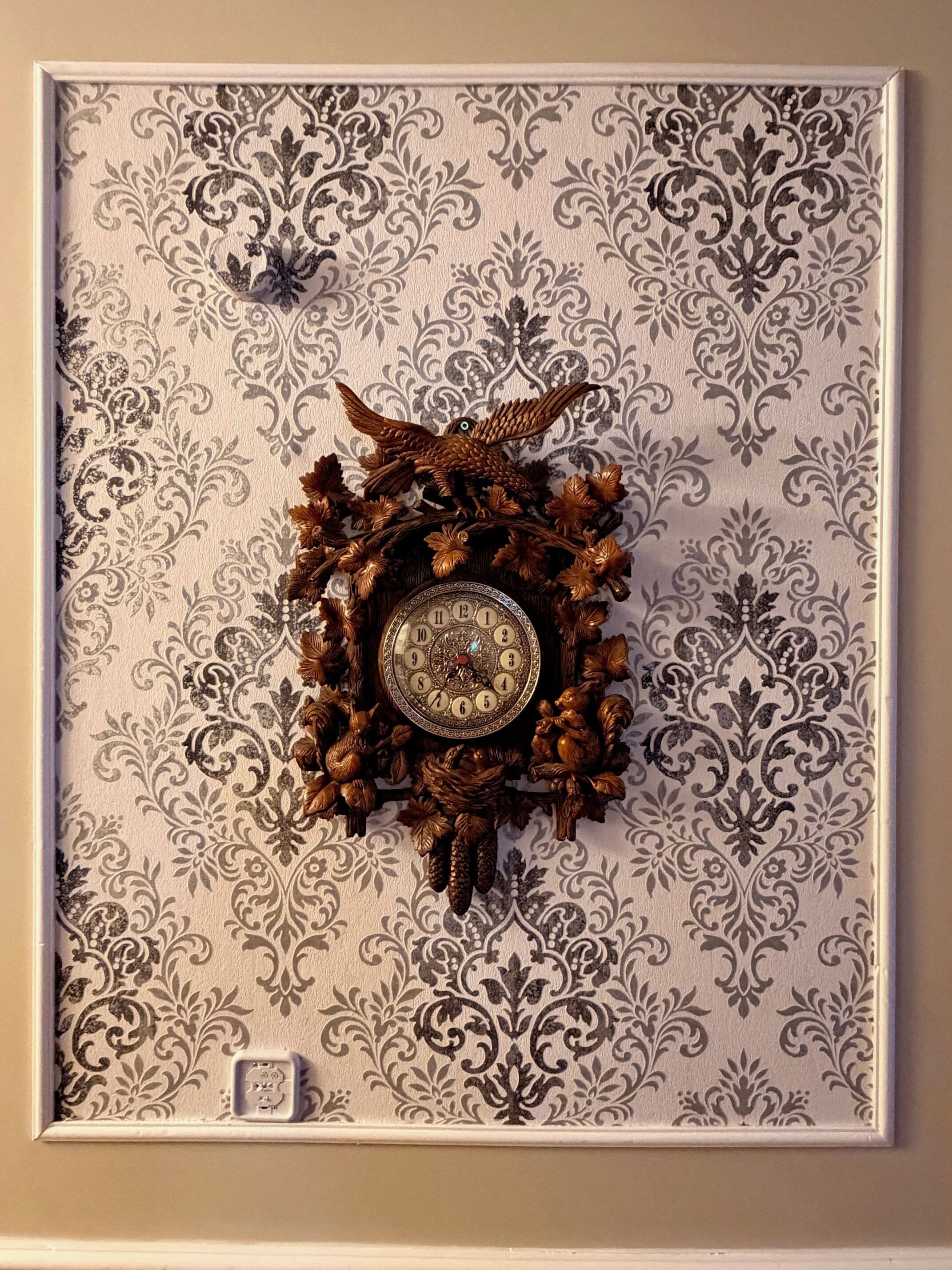 A wall-mounted cuckoo clock with intricate designs and a bird figure on top, set against a patterned wallpaper background.