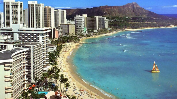 A coastal cityscape with high-rise buildings, a beach, and a mountain in the background. - Waikiki Banyan 1BR Condos with No Parking (Honolulu)