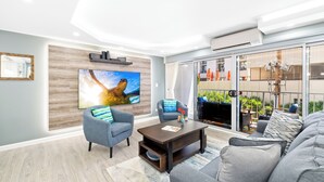 Ein modernes Wohnzimmer mit einem großen Flachbildfernseher, grauen Sofas und einem Couchtisch.