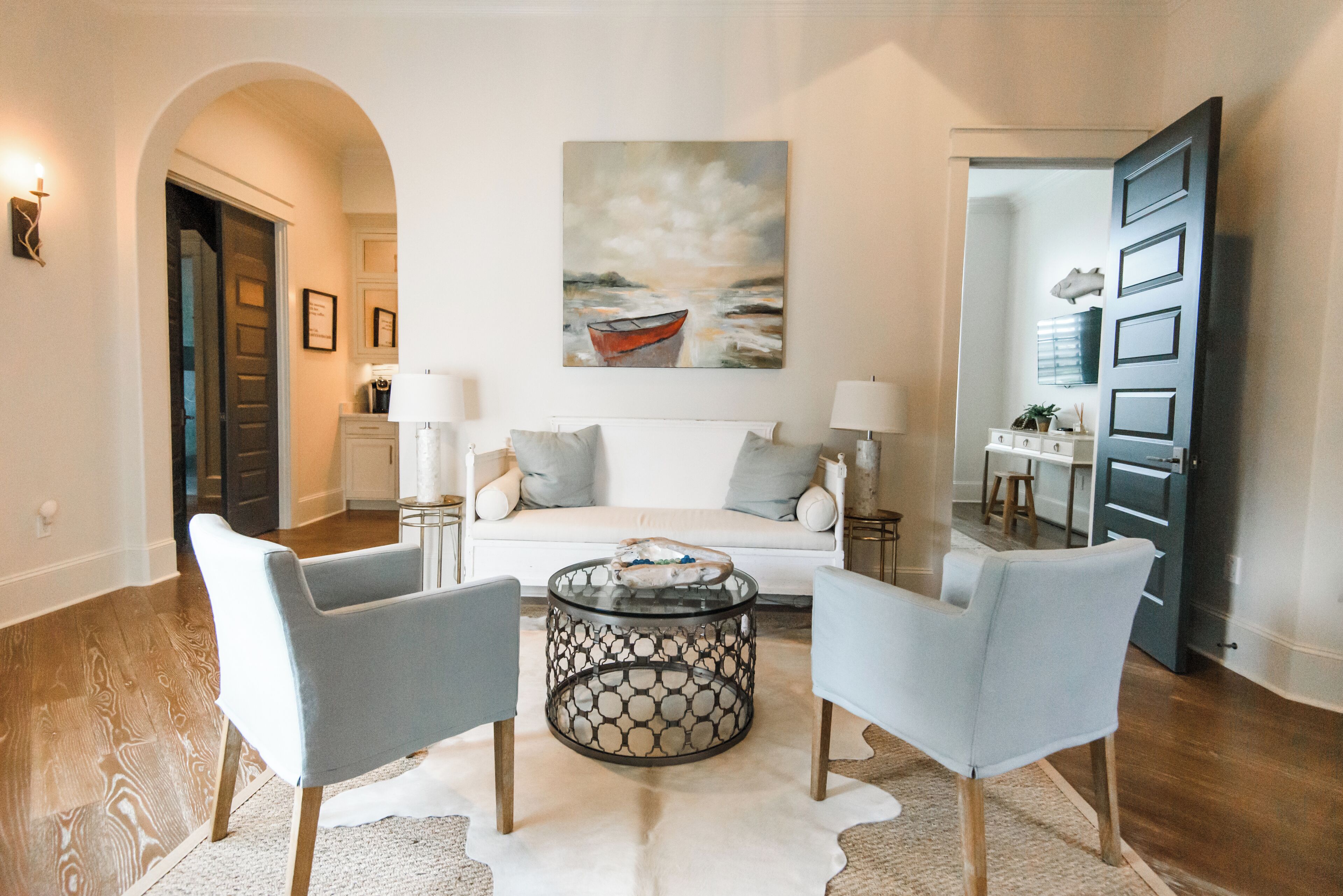 Un salon comprenant un canapé, deux fauteuils, une table basse et un tableau représentant un bateau accroché au mur.
