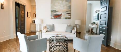 Un salon comprenant un canapé, deux fauteuils, une table basse et un tableau représentant un bateau accroché au mur.