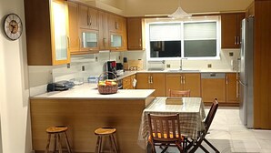 Una cocina moderna con armarios de madera, una isla central con taburetes, una mesa de comedor con sillas y un amplio ventanal que proporciona luz natural.
