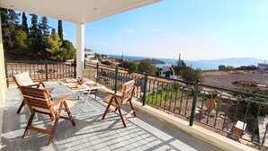 Un balcón con una mesa lista para dos personas, con vistas a un paisaje costero que incluye el mar y colinas lejanas.