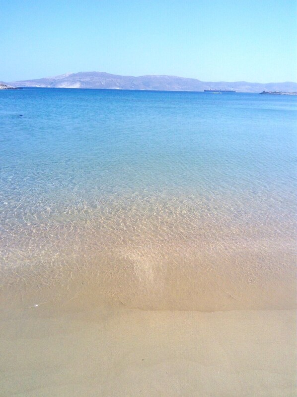 A clear beach with calm water and distant mountains.