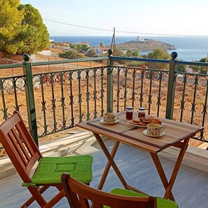 Un balcón con una mesa dispuesta para dos, una silla y vistas al mar y edificios a la distancia.