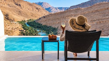 Una persona asseguda a taula, al costat d'una piscina, amb vista a un paisatge de muntanya.