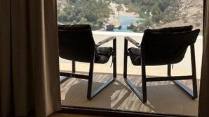 A room with a large window overlooking a mountainous landscape. There are two black chairs and a small table in front of the window. - WADINA RESORT   (Wadi Bani Khalid)