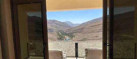 A room with a glass door leading to a balcony with two chairs and a table.