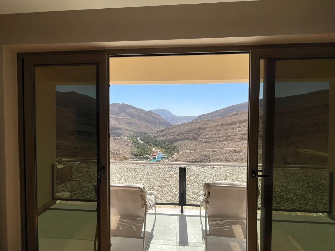 A room with a sliding glass door leading to a balcony with two chairs and a view of a mountainous landscape.