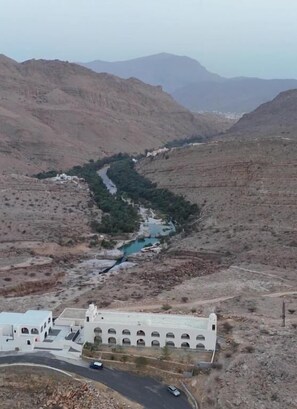 A white building with arched windows and a road leading to it. - WADINA RESORT   (Wadi Bani Khalid)