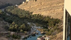 A modern building with a curved balcony overlooking a valley with a river and greenery. - WADINA RESORT   (Wadi Bani Khalid)