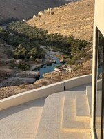 Un edificio moderno con un balcón curvo que da a un valle con río y vegetación.