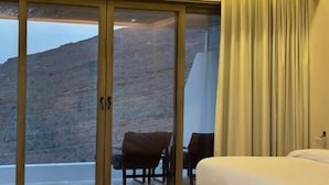 A hotel room with a large sliding glass door leading to a balcony, a bed, and a seating area with a table and chairs. - WADINA RESORT   (Wadi Bani Khalid)