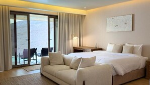 A hotel room with a large bed, a sofa, a desk, and a view through a sliding door. - WADINA RESORT   (Wadi Bani Khalid)