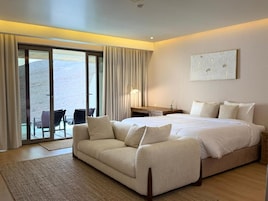 Una habitación de hotel con una cama grande, un sofá, un escritorio y vistas a través de un ventanal corredera.