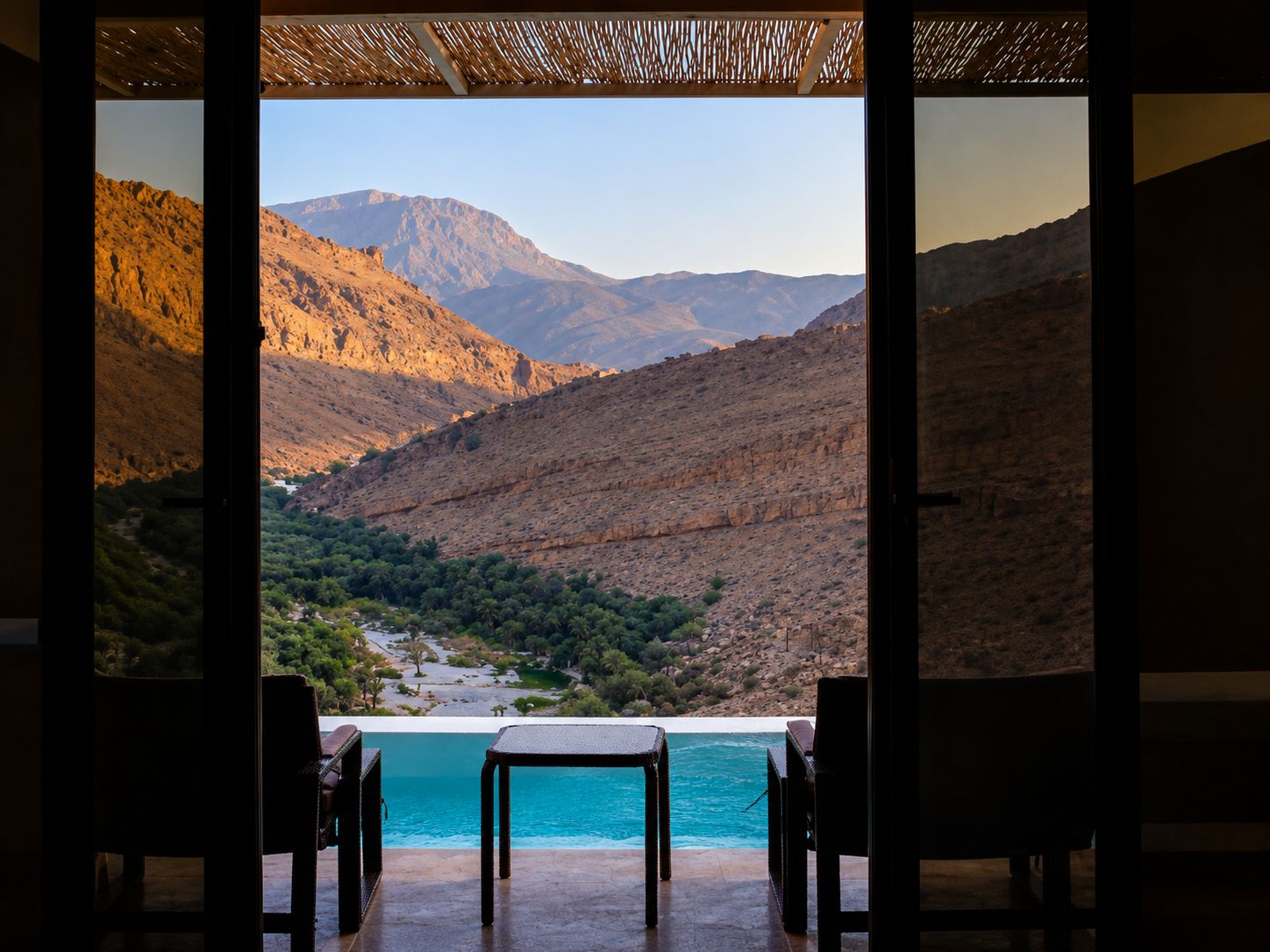 An outdoor seating area with a table and chairs overlooking a pool and a mountainous landscape.