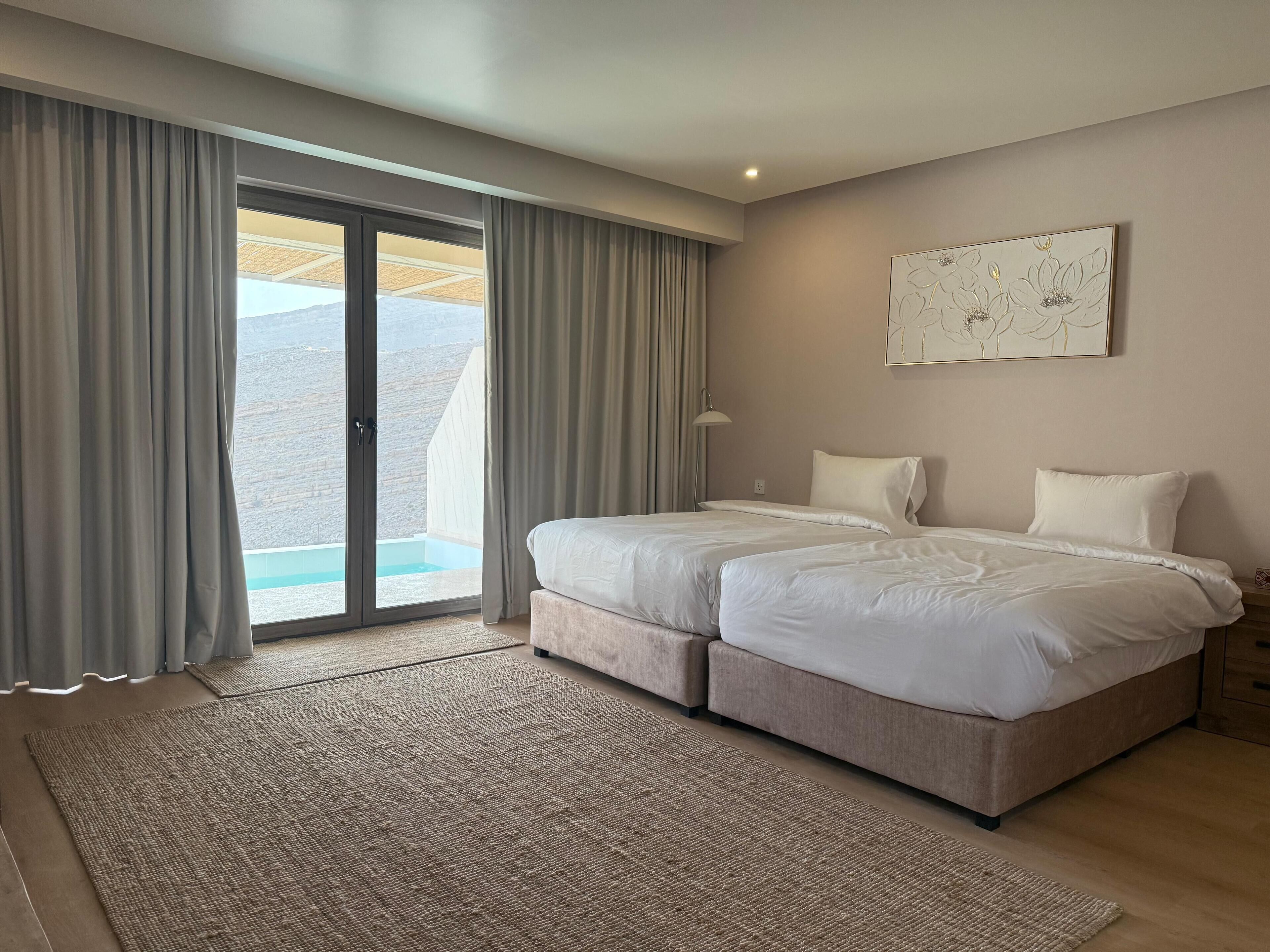Cama doble con cabecera, mesita de noche, lámpara y vistas a una piscina a través de un ventanal corredero.