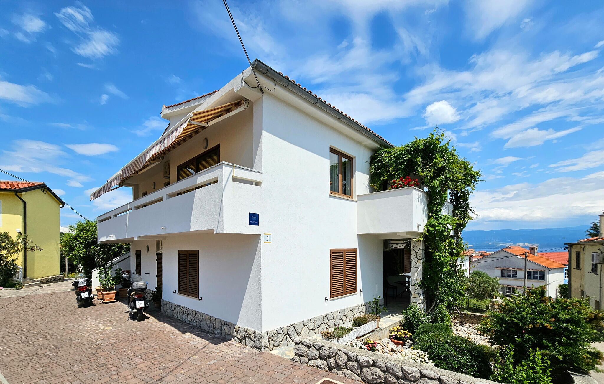 A two-story building with a white facade, stone foundation, and a tiled roof.
