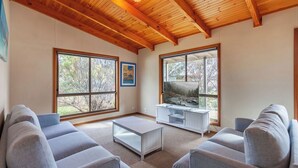 A living room with a wooden ceiling, large windows, a white entertainment unit, and grey sofas.