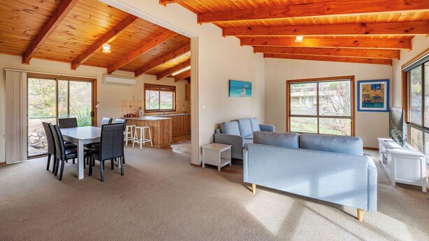 A spacious living area with a wooden ceiling, a dining table with chairs, a sofa, and a television.