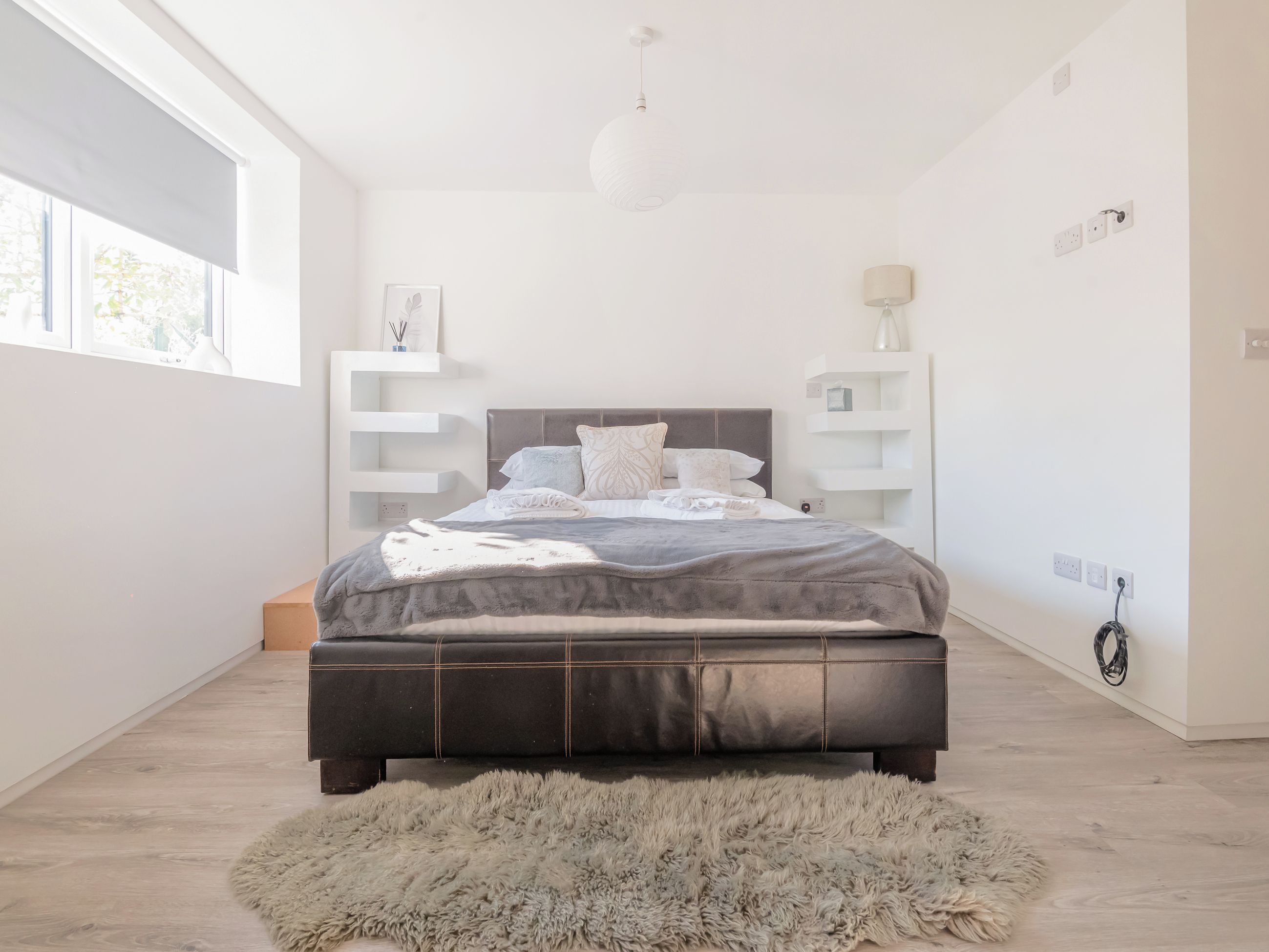 Ein modernes Schlafzimmer mit einem großen Bett, Einbauschränken, einem flauschigen Teppich und einer Pendelleuchte.
