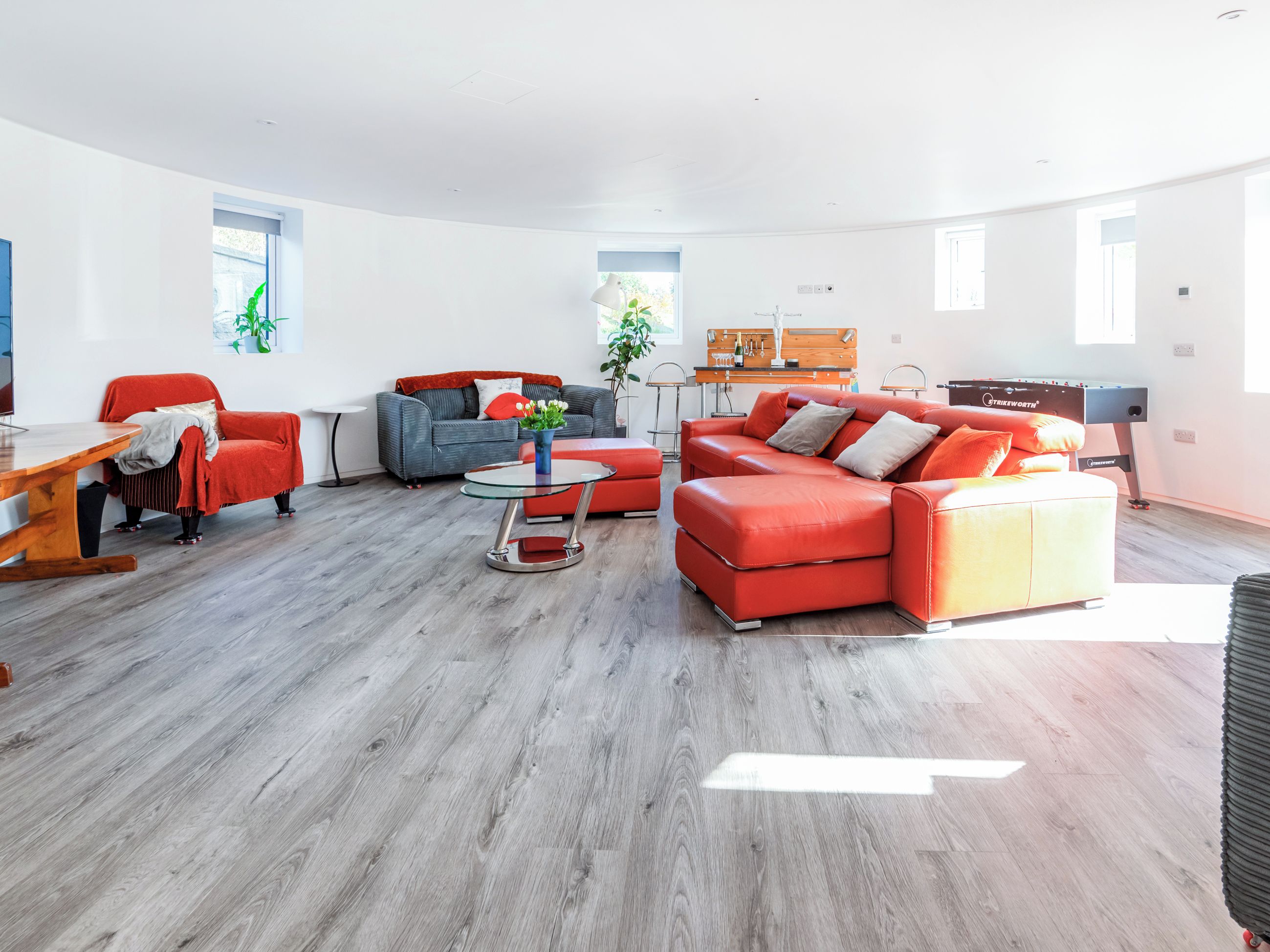 A modern living room with a sofa, armchair, coffee table, and a foosball table.