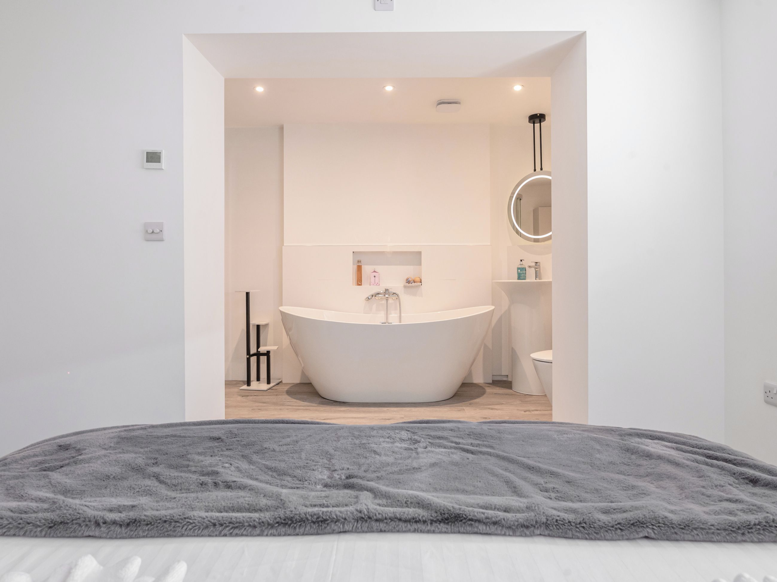 A modern bathroom with a freestanding bathtub, a round mirror, and a toilet.