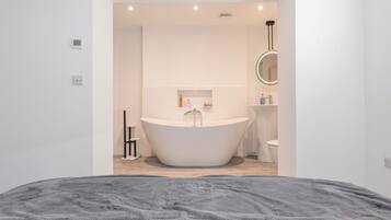 A modern bathroom with a freestanding bathtub, a round mirror, and a toilet.