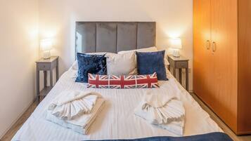 A neatly made bed with pillows, a headboard, bedside tables with lamps, and a wardrobe.