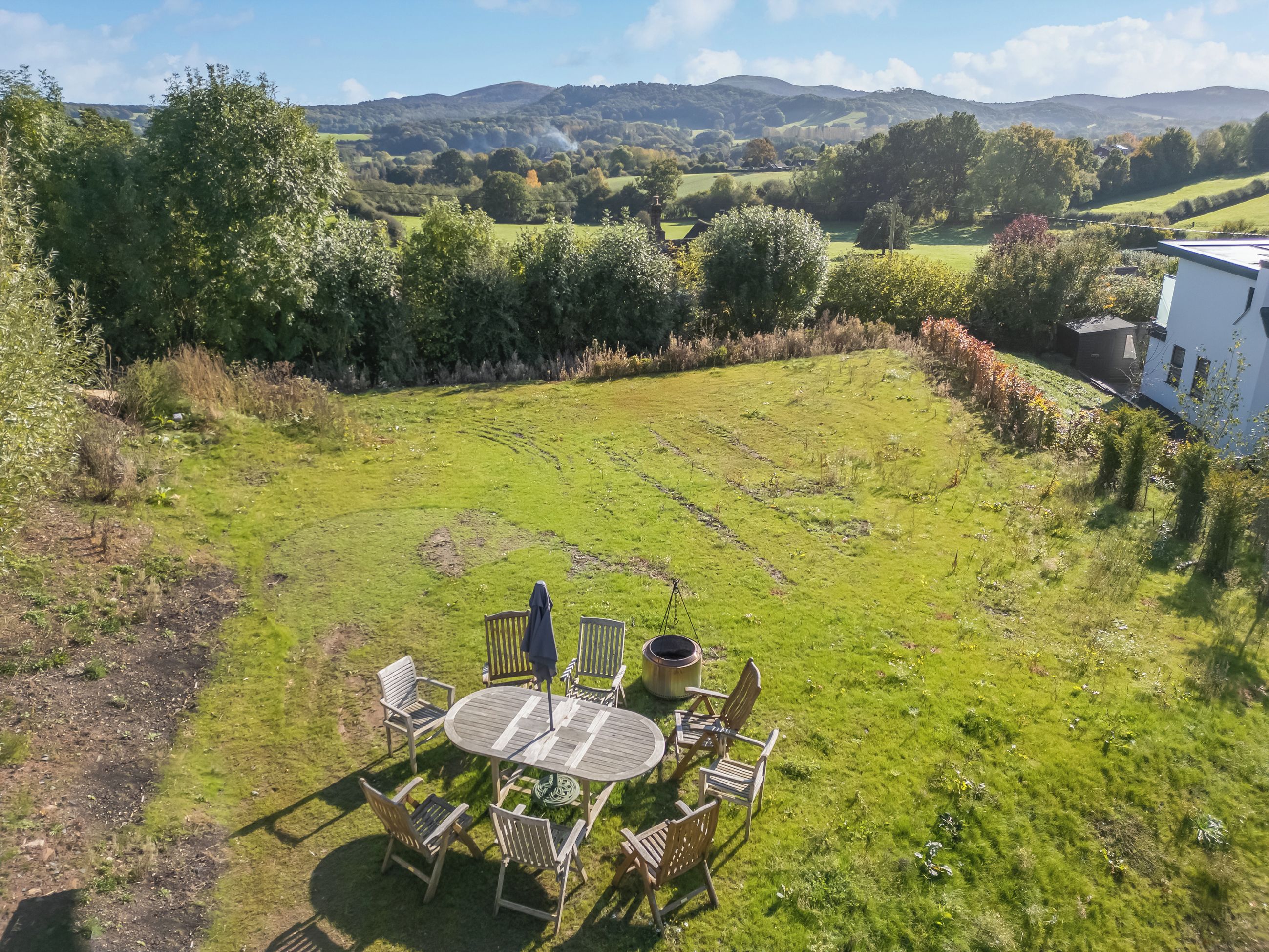 Un espace extérieur verdoyant avec une table ronde et des chaises, entouré d’arbres et offrant une vue sur des collines.