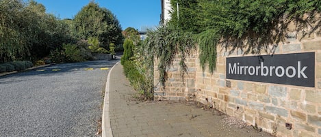 A paved walkway, a stone wall, and a sign reading 'Mirrorbrook.'