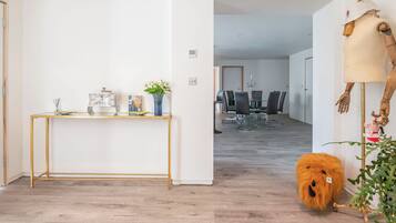 A modern interior with a wooden floor, a glass-top console table, a dining area with a chandelier, and a unique wooden sculpture.