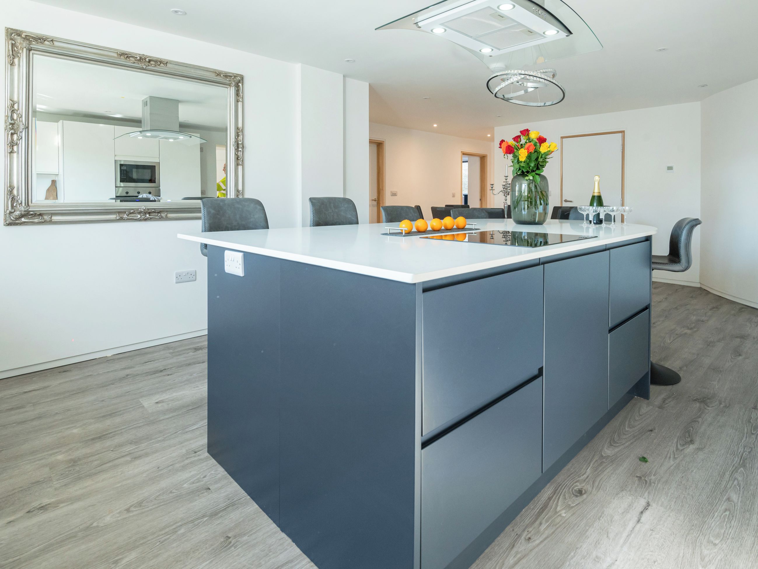 A modern kitchen with a central island, a large mirror, and a dining area with chairs.