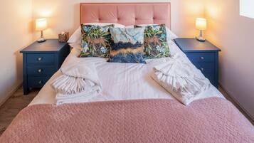 Una cama bien hecha con colcha rosa, dos mesitas de noche con lámparas y almohadones decorativos.