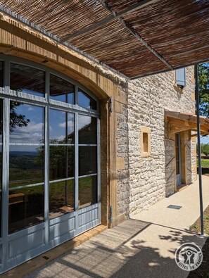 A stone building with large windows and a wooden pergola. - La Maison du Crêt - RIVOLET (RIVOLET)