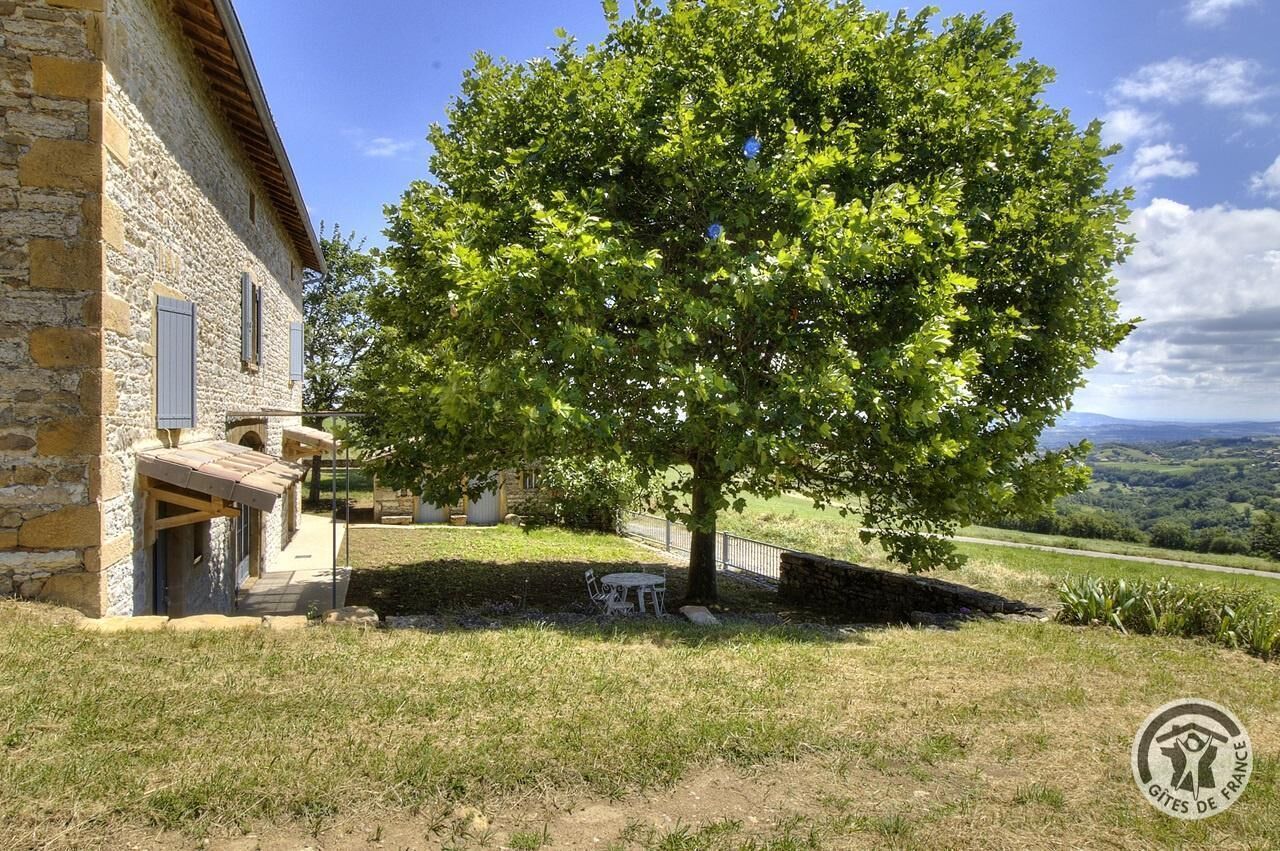 Ein Steinhäuschen mit Baum davor, einem Tisch und Stühlen.