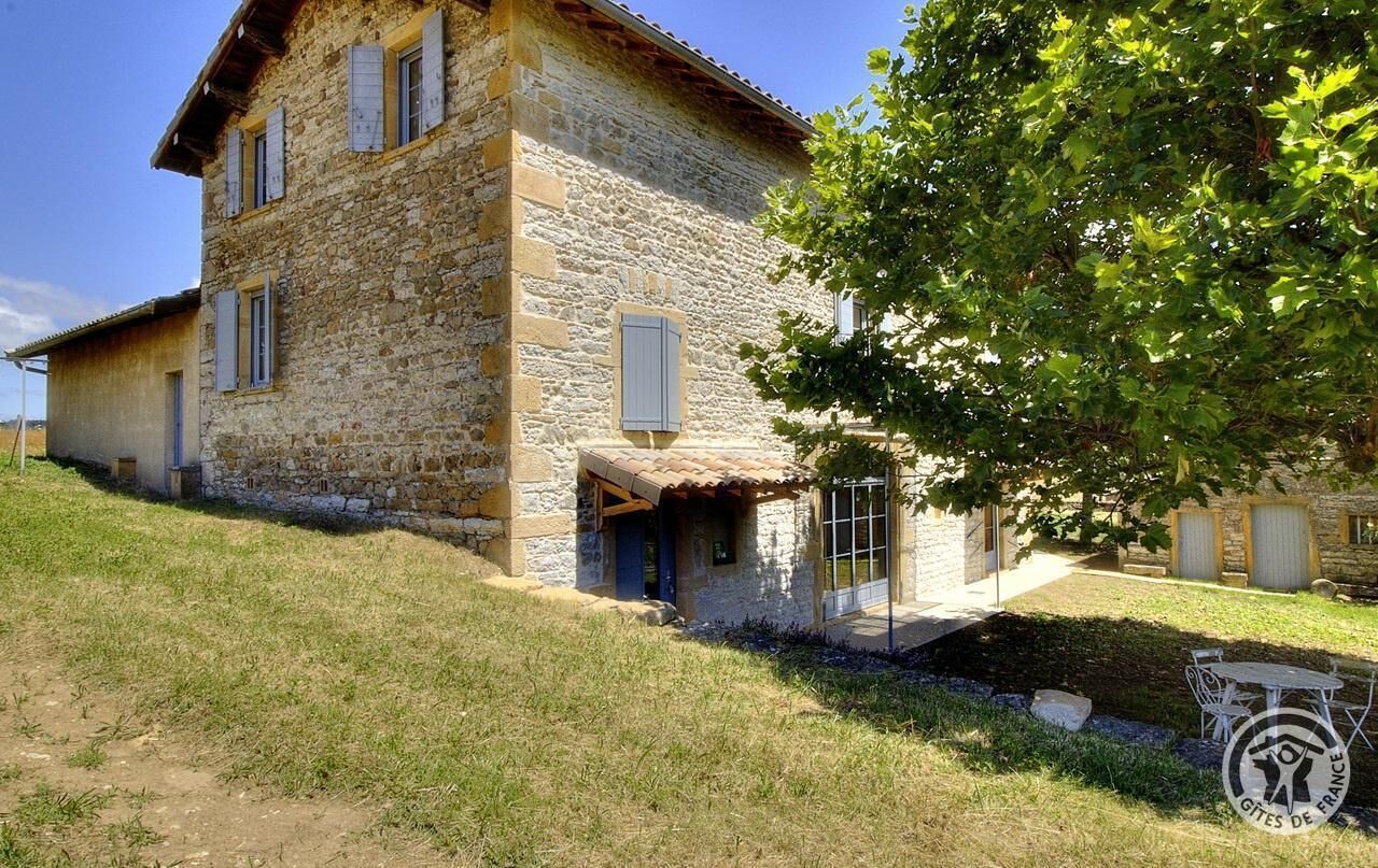 A stone building with a sloped roof, a small porch, and a tree in the foreground.