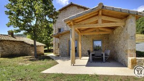 A stone building with a covered patio area, outdoor seating, and a view of the surrounding landscape. - La Maison du Crêt - RIVOLET (RIVOLET)
