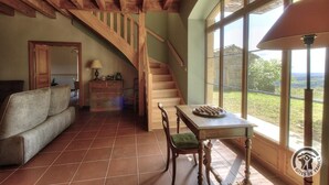 A spacious living area with a wooden staircase, a dining table with a board game, and a view through large windows. - La Maison du Crêt - RIVOLET (RIVOLET)